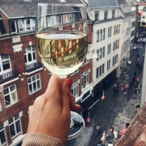 A glass of white wine held from a rooftop overlooking Copenhagen